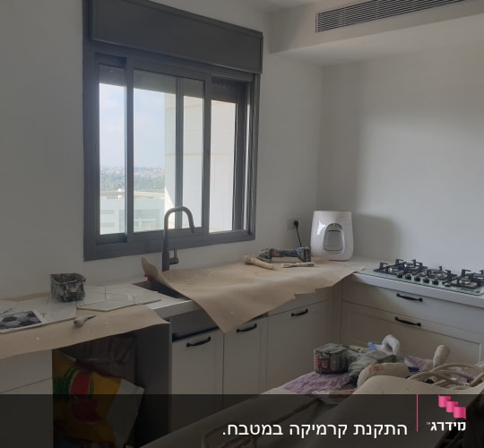 מטבח בשיפוץ עם ניירות מגן וכלי עבודה על השיש